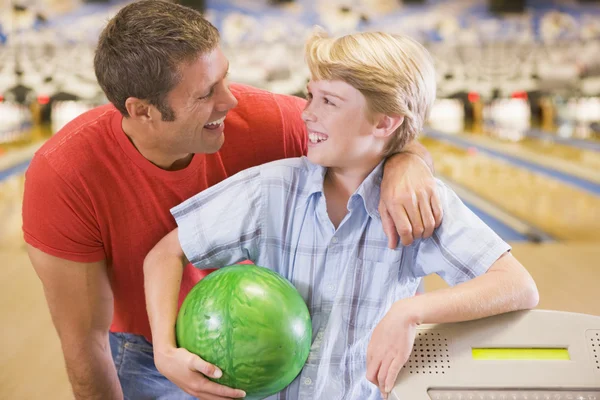 Man and young boy in bowling alley holding ball and smiling Stock Picture