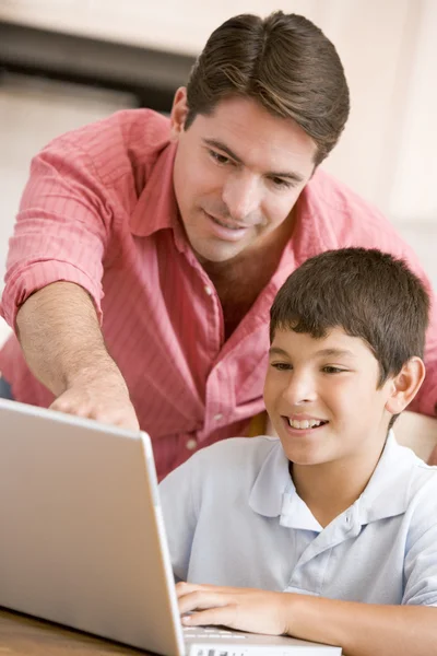 Man helping young boy in kitchen with laptop smiling — Stock Photo, Image