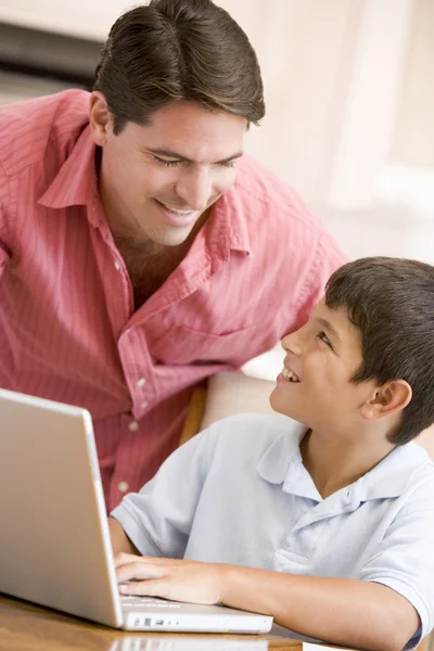 Man helping young boy in kitchen with laptop smiling — Stock Photo, Image