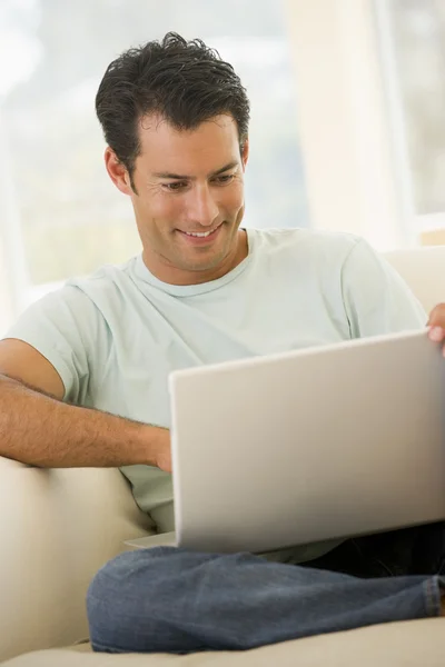 Hombre en la sala de estar usando el ordenador portátil sonriendo Imágenes de stock libres de derechos
