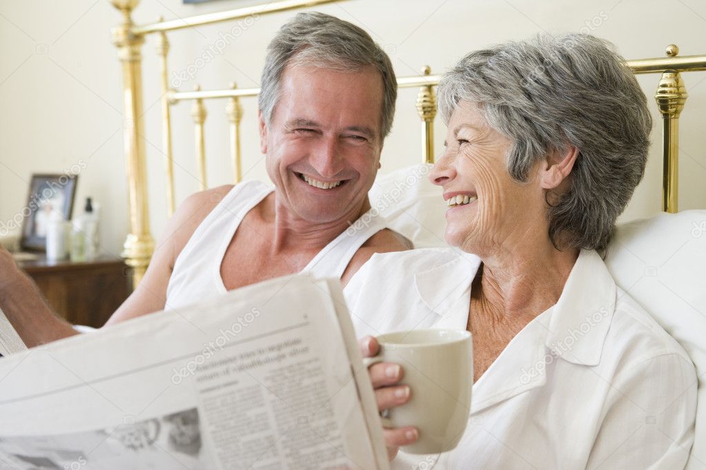 Couple In Bedroom Mit Kaffee Und Zeitung Lacheln Stockfoto