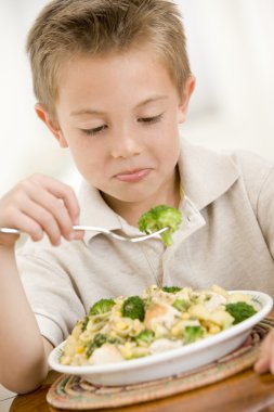 Young boy indoors eating pasta with brocoli clipart