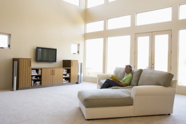 Man reading book in living room smiling clipart