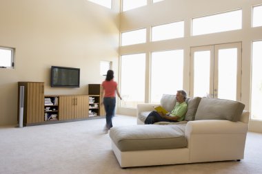 Man reading book in living room with woman walking by clipart