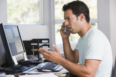 Man in home office on telephone using computer and frowning clipart