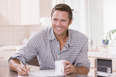 Man in kitchen reading newspaper and smiling clipart