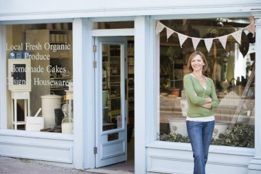 Woman standing in front of organic food store smiling clipart