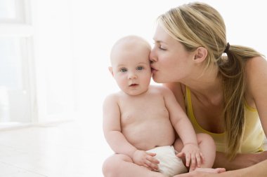 Mother kissing baby indoors clipart