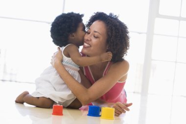 Mother and daughter indoors kissing and smiling clipart