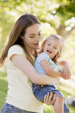 Mother holding daughter outdoors smiling clipart
