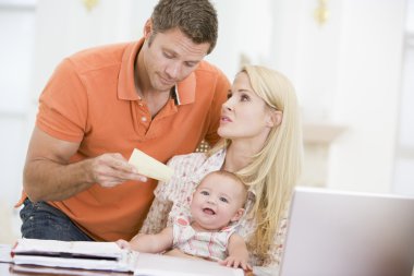 Couple and baby in dining room with laptop and paperwork clipart