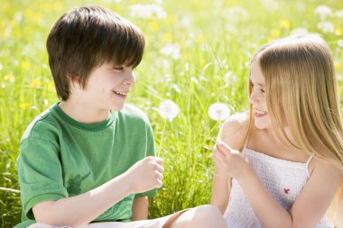 Two young children sitting outdoors holding dandelion heads smil clipart