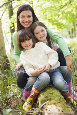 Mother and daughters outdoors in woods sitting on log smiling clipart