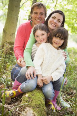 Family outdoors in woods sitting on log smiling clipart