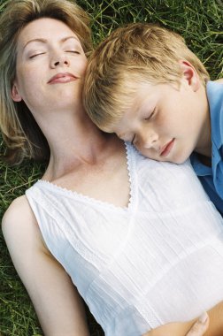 Mother and son lying outdoors sleeping clipart