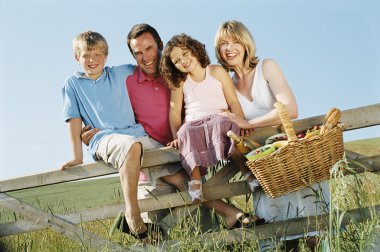 Family outdoors by fence with picnic basket smiling clipart