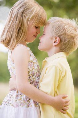 Two young children hugging outdoors clipart