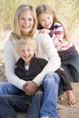 Mother and two young children sitting on beach smiling clipart