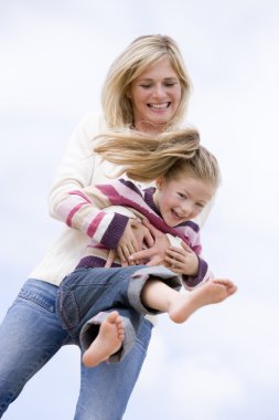 Mother and daughter playing on beach smiling clipart