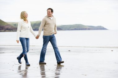 Couple walking on beach holding hands smiling clipart