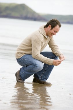 Man crouching on beach smiling clipart