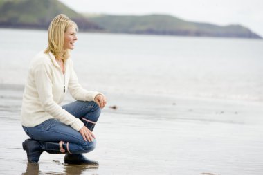 Woman crouching on beach smiling clipart