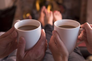 Feet warming at fireplace with hands holding coffee clipart