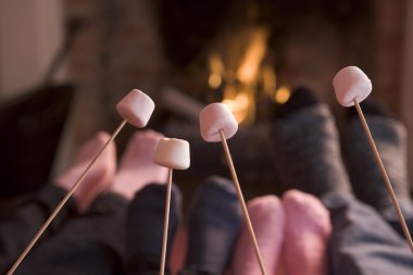 Feet warming at a fireplace with marshmallows on sticks clipart
