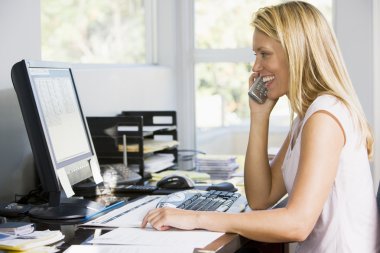 Woman in home office with computer using telephone smiling clipart