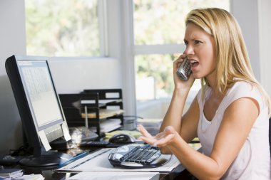 Woman in home office with computer using telephone frowning clipart