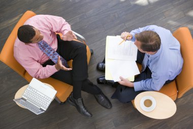 Two businessmen sitting indoors with coffee laptop and folder clipart