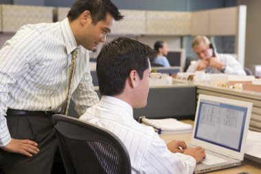 Two businessmen in cubicle looking at laptop clipart