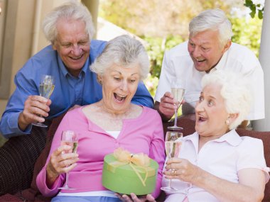 Two couples on patio with champagne and gift smiling clipart