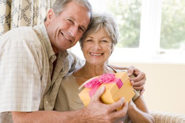 Husband giving wife gift in living room smiling clipart