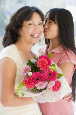 Granddaughter kissing grandmother on cheek holding flowers and s clipart