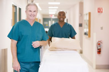 Two Orderlies Pushing An Empty Bed Down A Hospital Corridor clipart