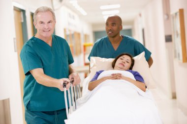 Two Orderlies Pushing A Woman In A Bed Down A Hospital Corridor clipart