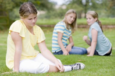 Two young girls bullying other young girl outdoors clipart