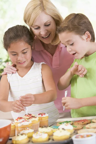 微笑のクッキーを飾る台所の 2 人の子供を持つ女性 — ストック写真