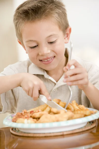 Jeune garçon à l'intérieur manger du poisson et des chips souriant — Photo