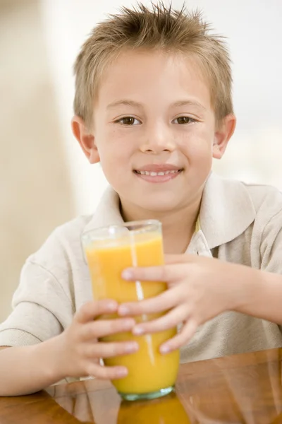 Young boy indoors with orange juice smiling — Stock Photo, Image