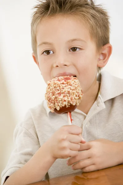 Young boy indoors eating candy apple — Stock Photo, Image
