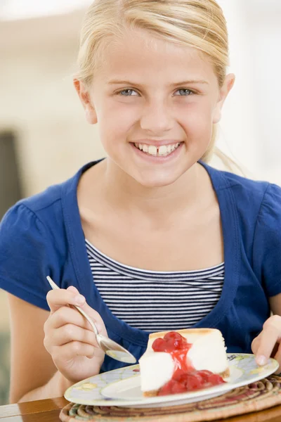 Νεαρό κορίτσι σε εσωτερικούς χώρους, τρώει cheesecake χαμογελώντας — Φωτογραφία Αρχείου