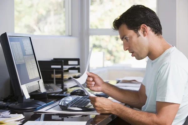 書類を保持していると見ているコンピューターを使用してホーム オフィスの男 — ストック写真
