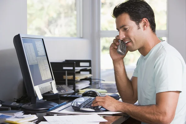 Hombre en la oficina en el teléfono usando la computadora y sonriendo —  Fotos de Stock