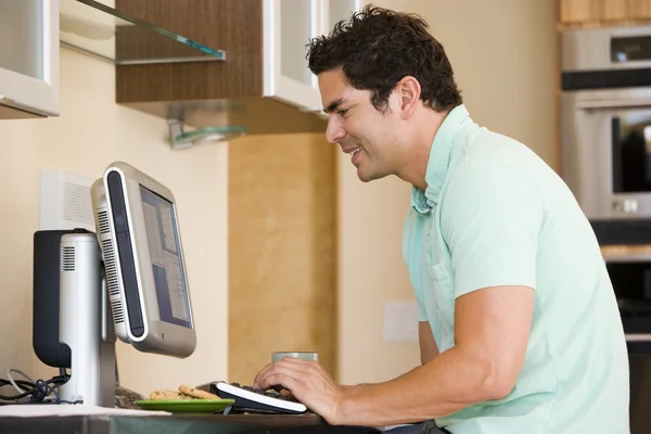 Homem na cozinha usando computador e sorrindo — Fotografia de Stock