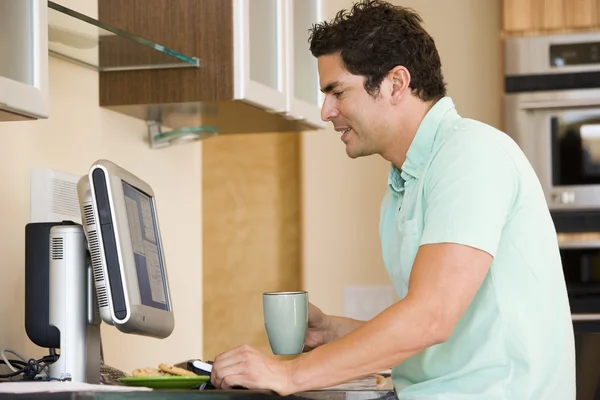 Człowiek w kuchni z kawą, przy użyciu komputera i uśmiechając się — Zdjęcie stockowe