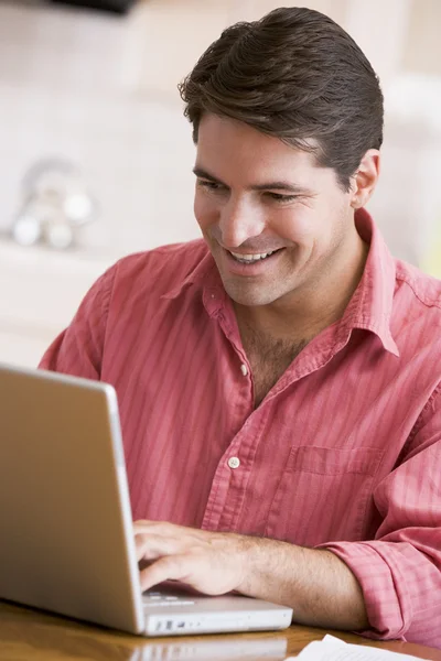 在厨房里使用的笔记本电脑微笑的男人 — 图库照片