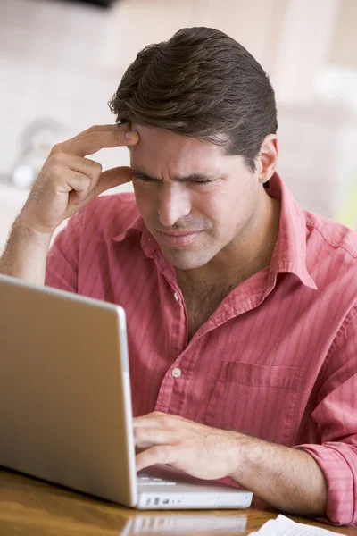 Homem na cozinha usando laptop franzindo a testa — Fotografia de Stock