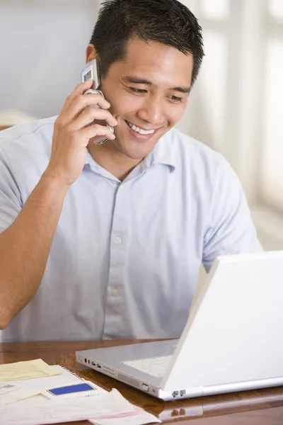 Чоловік в їдальні на мобільному телефоні, використовуючи ноутбук посміхаючись — стокове фото